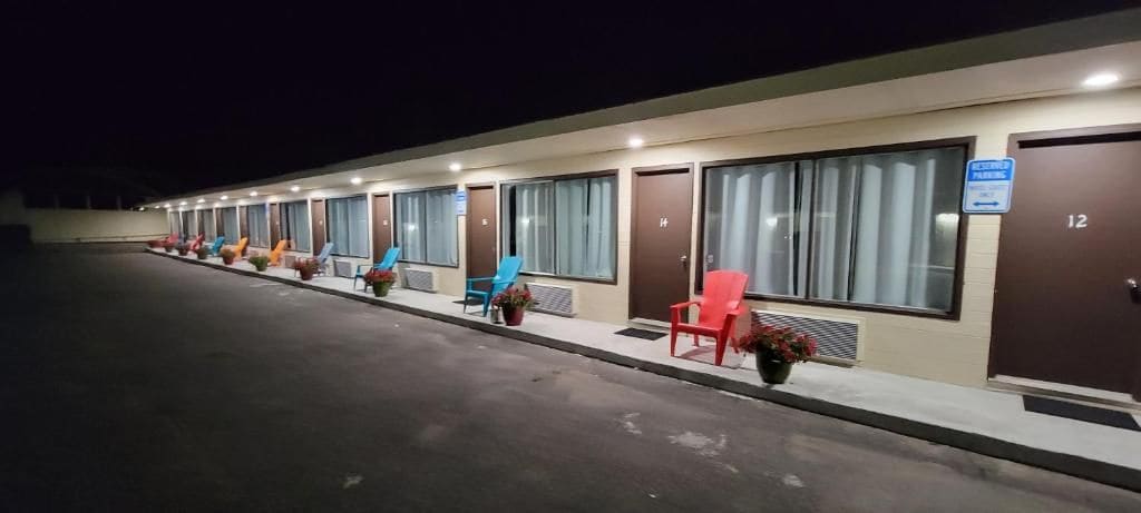 Un motel con habitaciones individuales, cada una con un número de puerta, una ventana y una silla afuera.