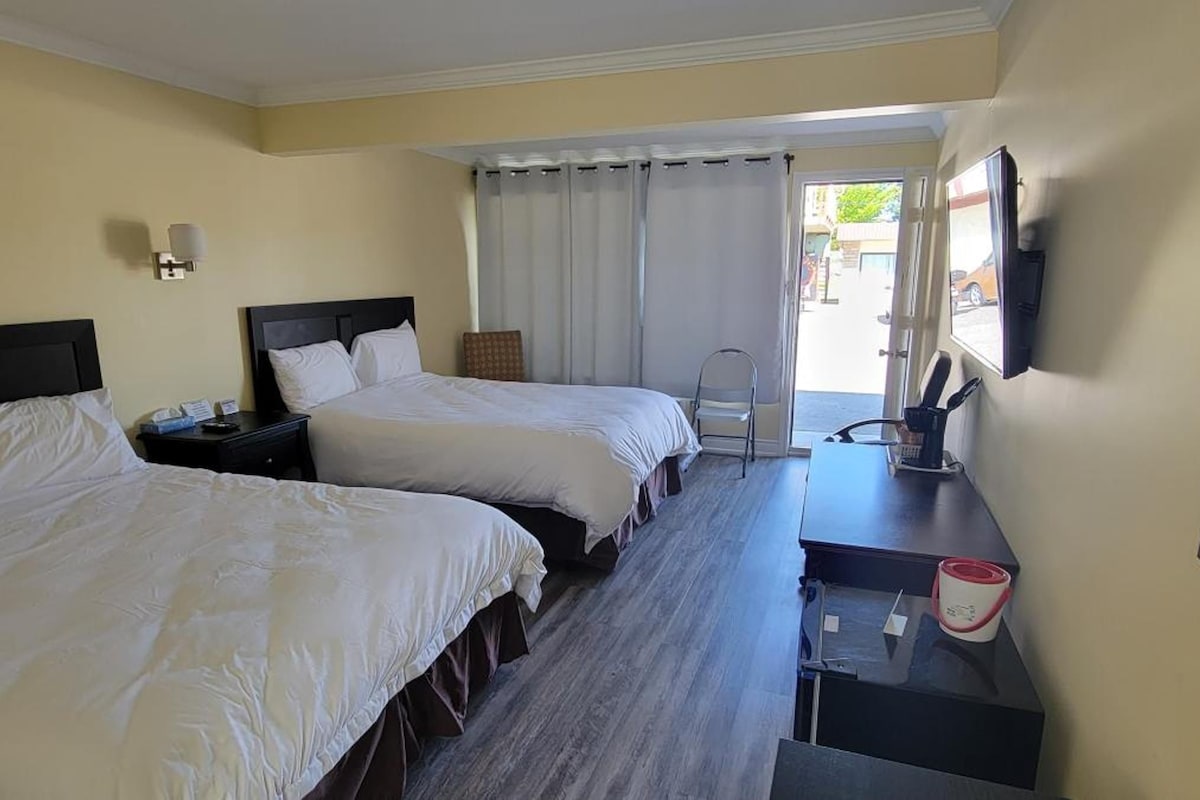 Une chambre d’hôtel avec deux lits, un bureau, une chaise, un miroir et une fenêtre avec des rideaux.