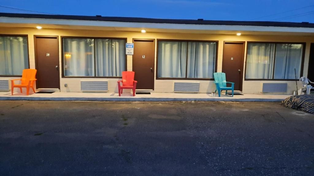 Un motel avec des chambres numérotées, un parking et des chaises à l’extérieur.