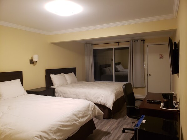 Habitación de hotel con dos camas, un escritorio con cafetera, televisión y puerta corredera que da a un balcón.