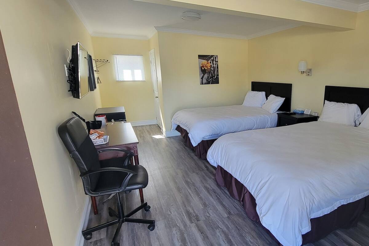 A hotel room with two beds, a desk with a chair, a small table, and a wall-mounted TV.