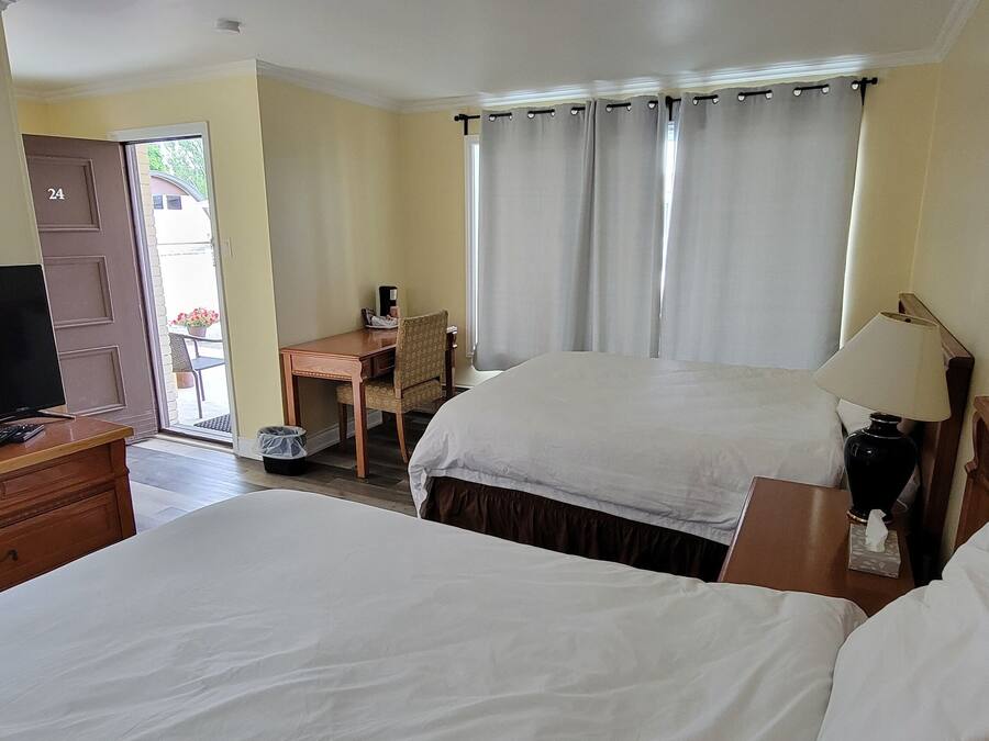 Une chambre d’hôtel avec deux lits, une télévision, un bureau et une fenêtre avec des rideaux.