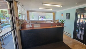 A reception area with a wooden counter, a TV mounted on the wall, and a large window with blinds. - North Shore Wayside Inn (Blind River)