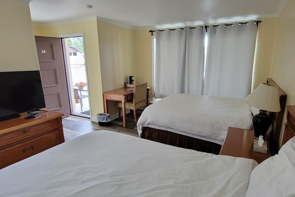 A hotel room with two beds, a desk, a television, and a window with curtains.