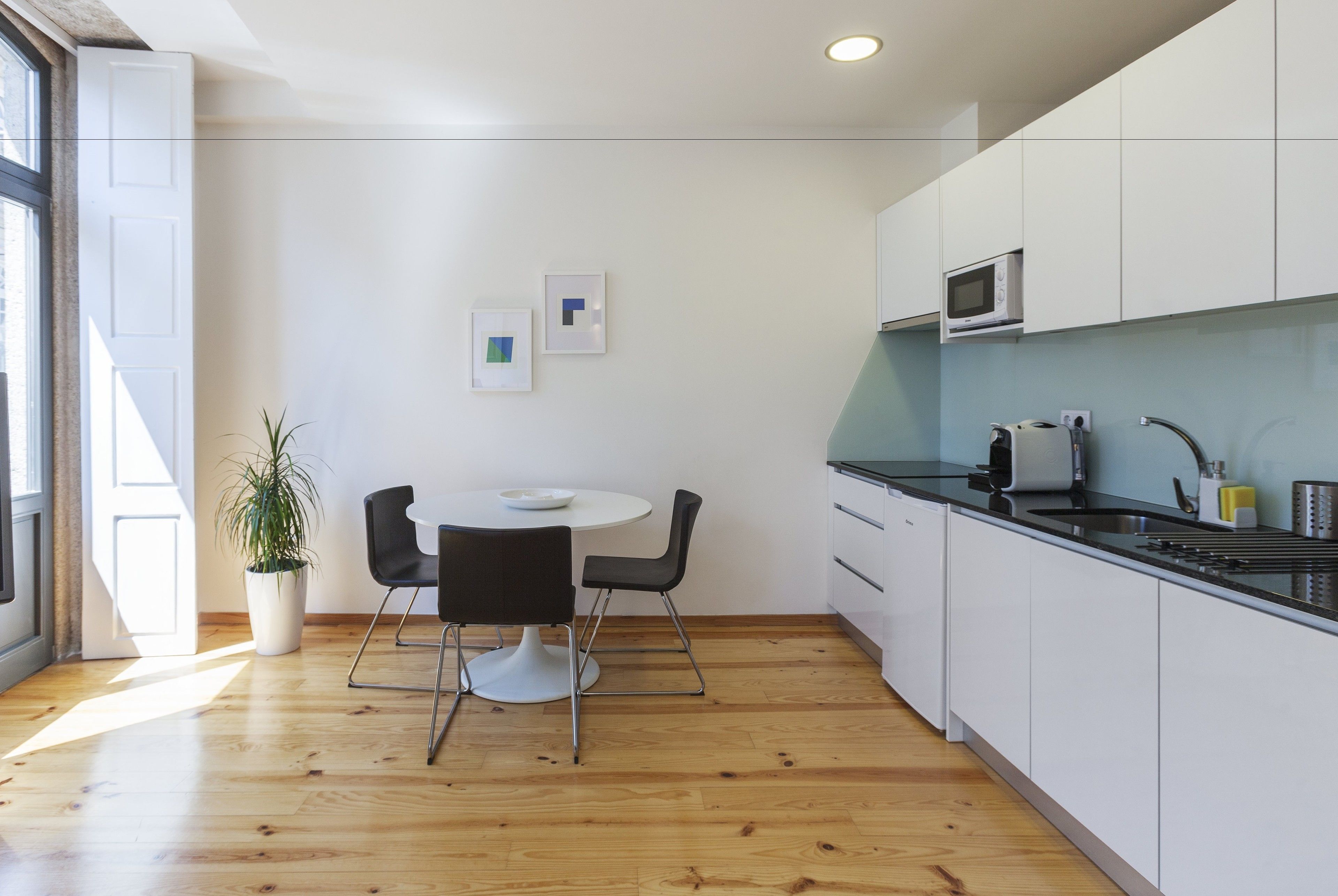 Une cuisine moderne avec des meubles blancs, un four à micro-ondes et un évier. On y trouve également un coin repas avec une table blanche et des chaises noires.