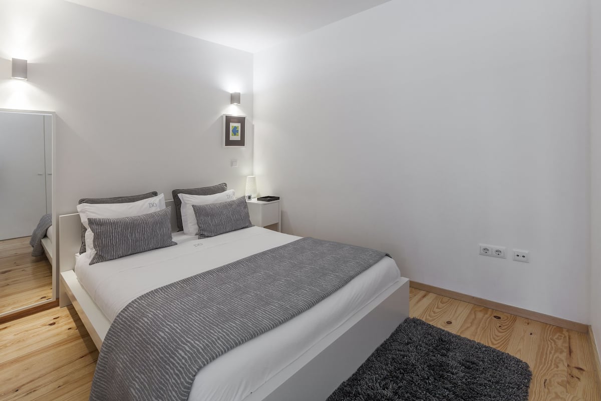 A modern bedroom with a large bed, bedside tables, and a wall-mounted light fixture.