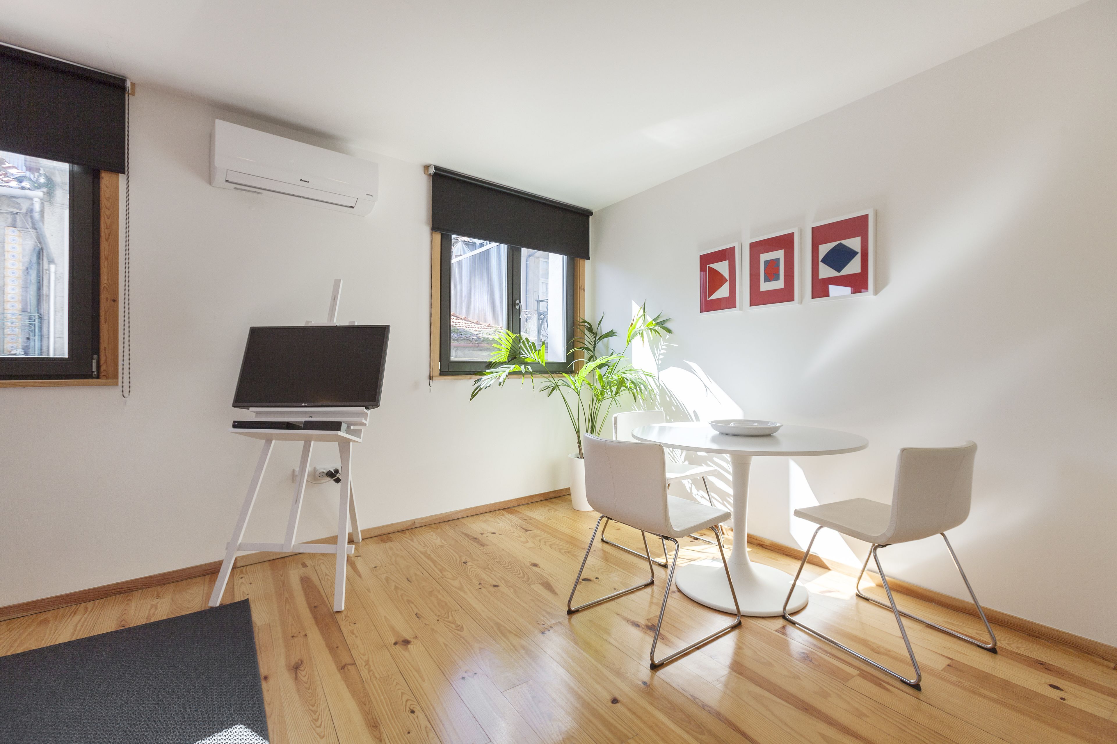 Una habitación moderna con un escritorio de pie, una mesa redonda, dos sillas, una planta en maceta y una obra de arte en la pared.