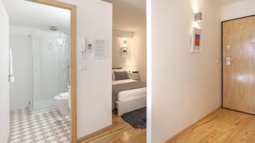 A modern hotel room with a glass shower enclosure, a bed with a gray blanket, and a wooden door.