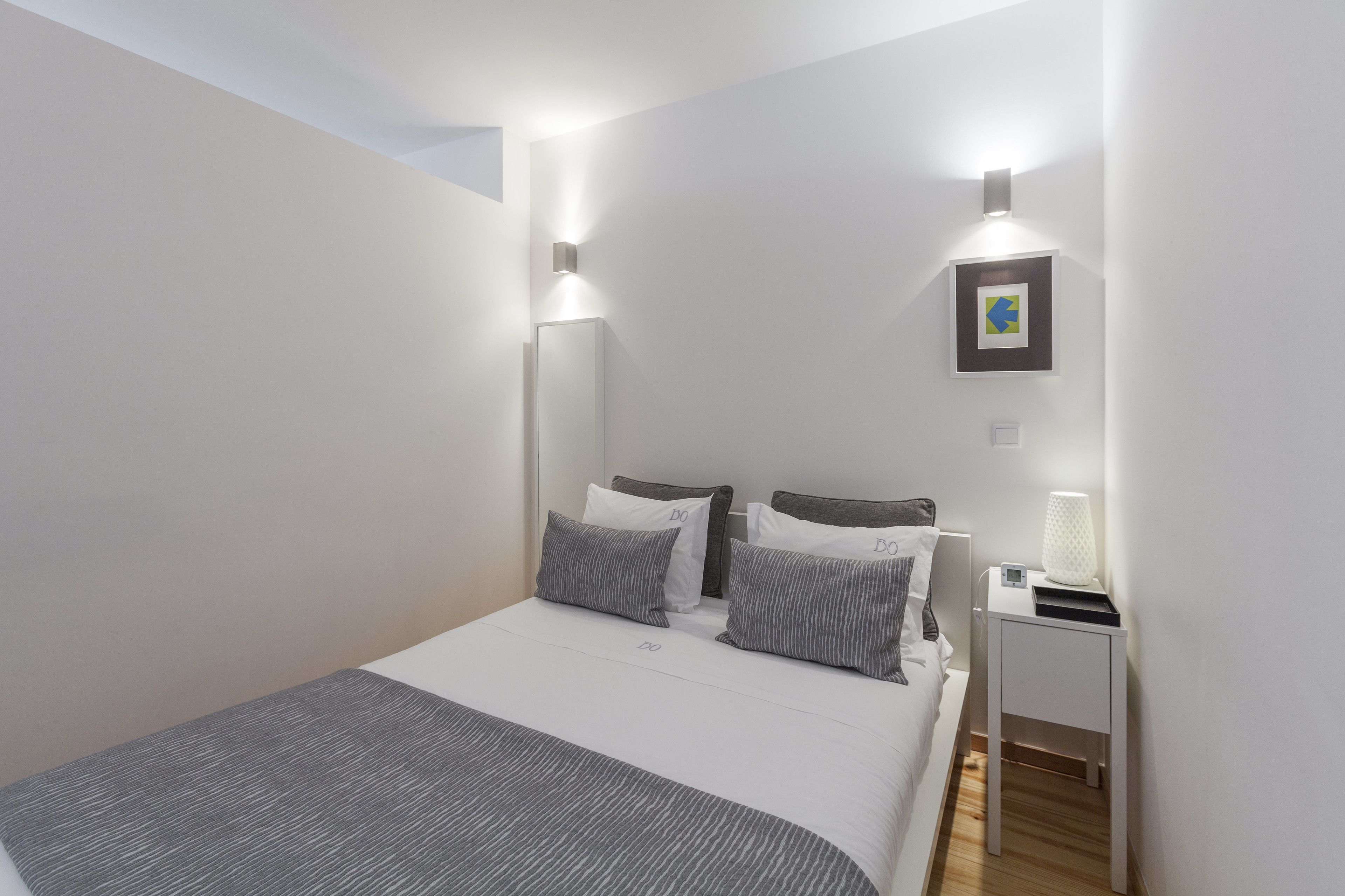 A modern bedroom with a neatly made bed, two bedside tables, and a wall-mounted light fixture.