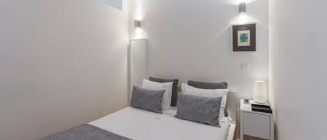 A modern bedroom with a neatly made bed, two bedside tables, and a wall-mounted light fixture.