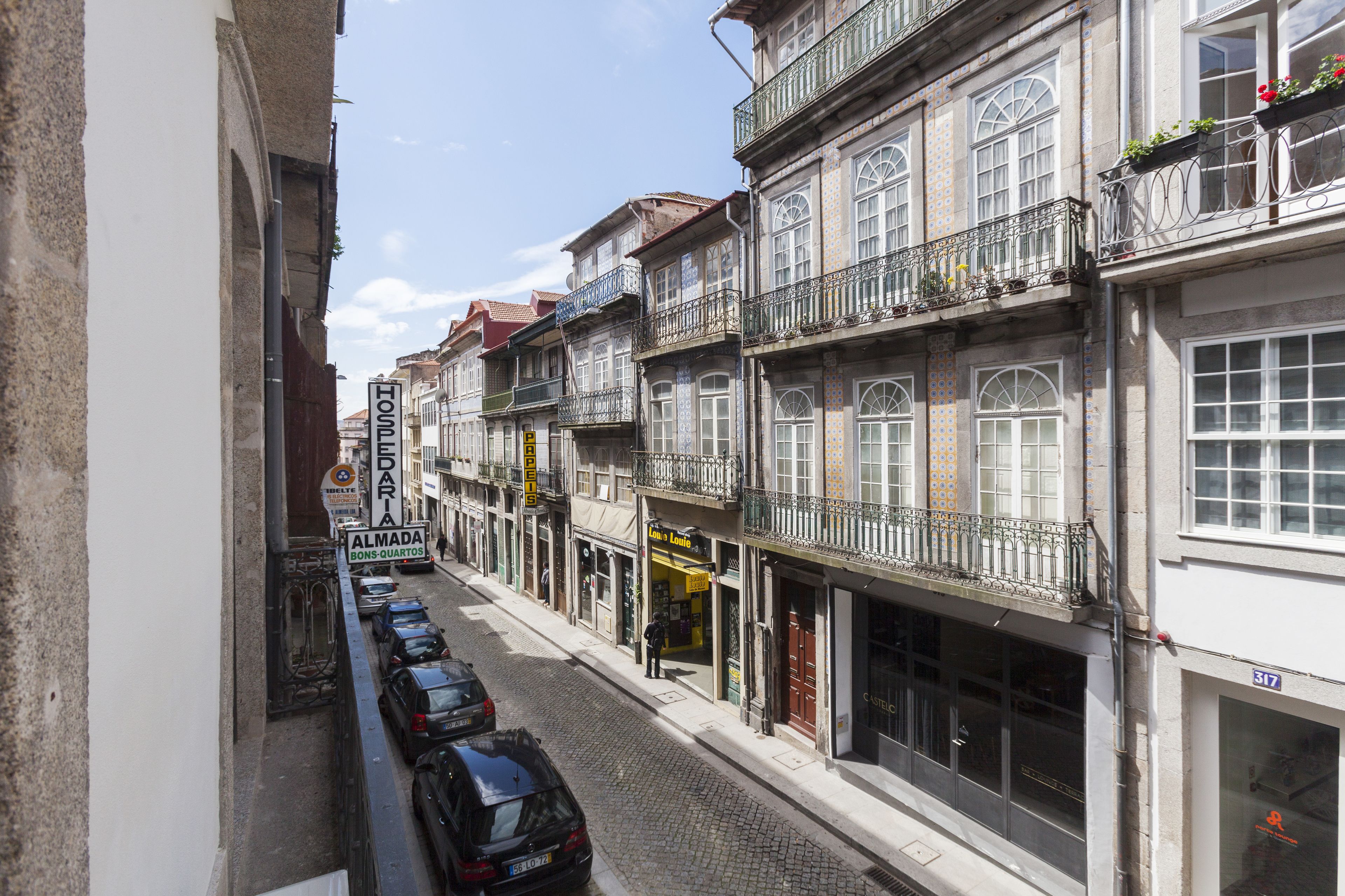 A narrow street lined with multi-story buildings, some with balconies and shops on the ground floor.