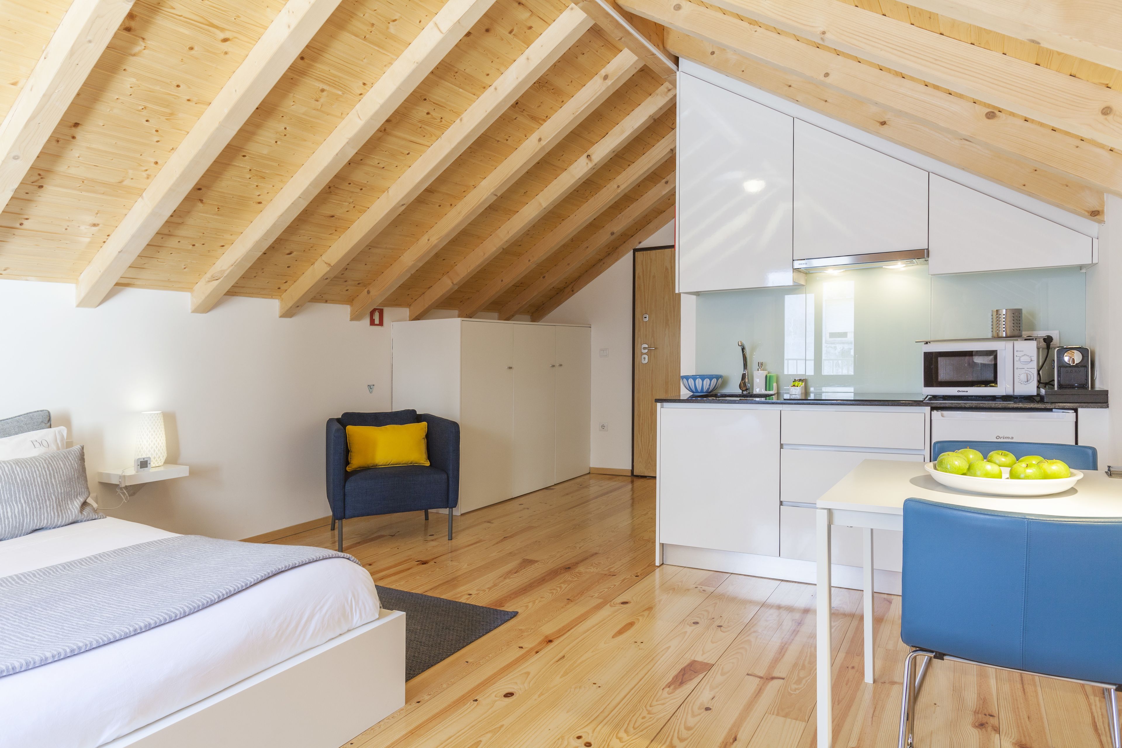 A compact, modern apartment with a loft-style kitchen, a dining area, and a bedroom.