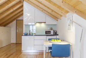 Una cocina moderna con armarios blancos, un microondas y una zona de comedor con mesa y silla azul.