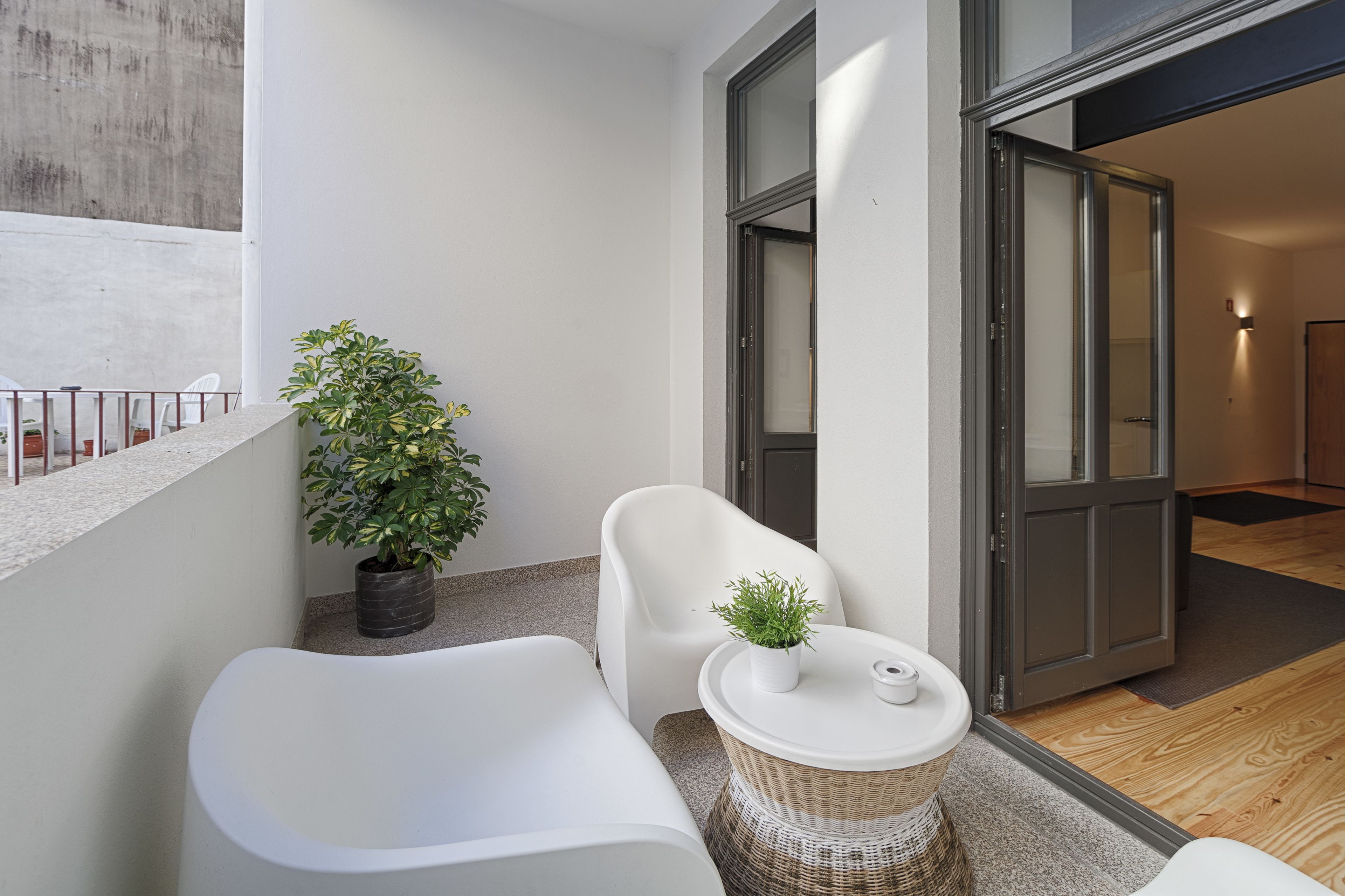 Un balcon moderne avec un canapé blanc, une petite table agrémentée d’un pot de fleurs et une table d’appoint en osier.