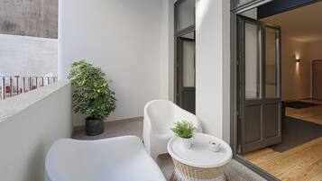 Un balcon moderne avec un canapé blanc, une petite table agrémentée d’un pot de fleurs et une table d’appoint en osier.