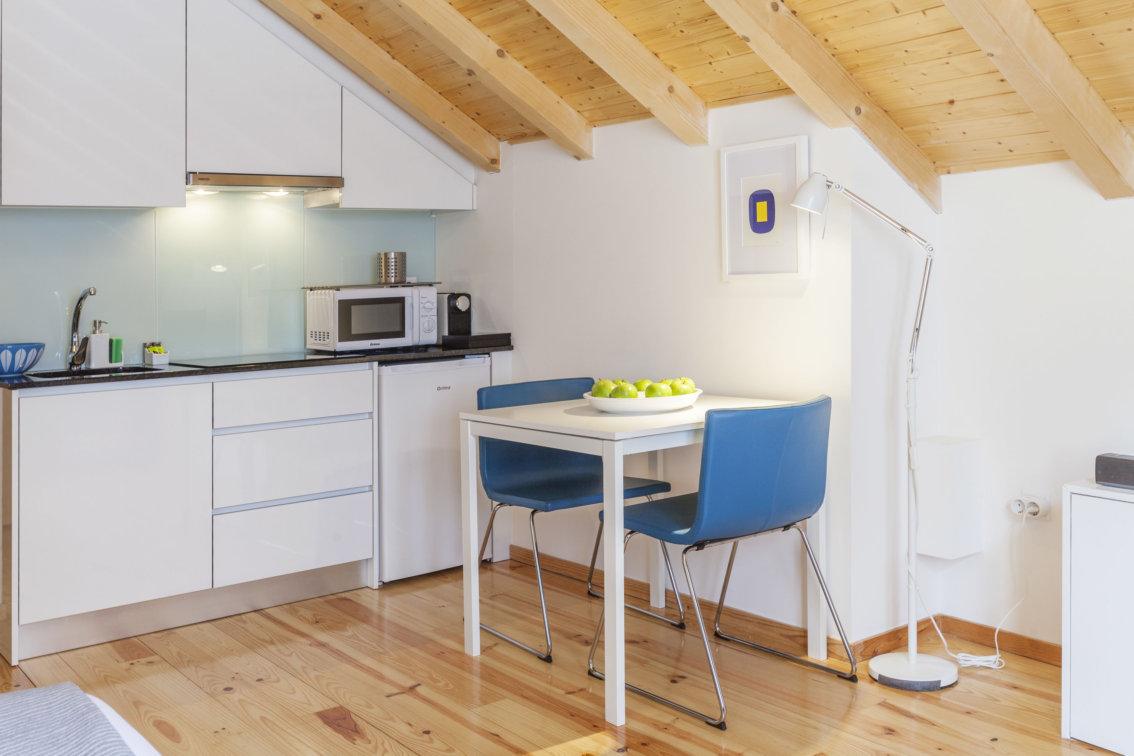 Una cocina moderna con armarios blancos, un microondas y una mesa de comedor con sillas azules.