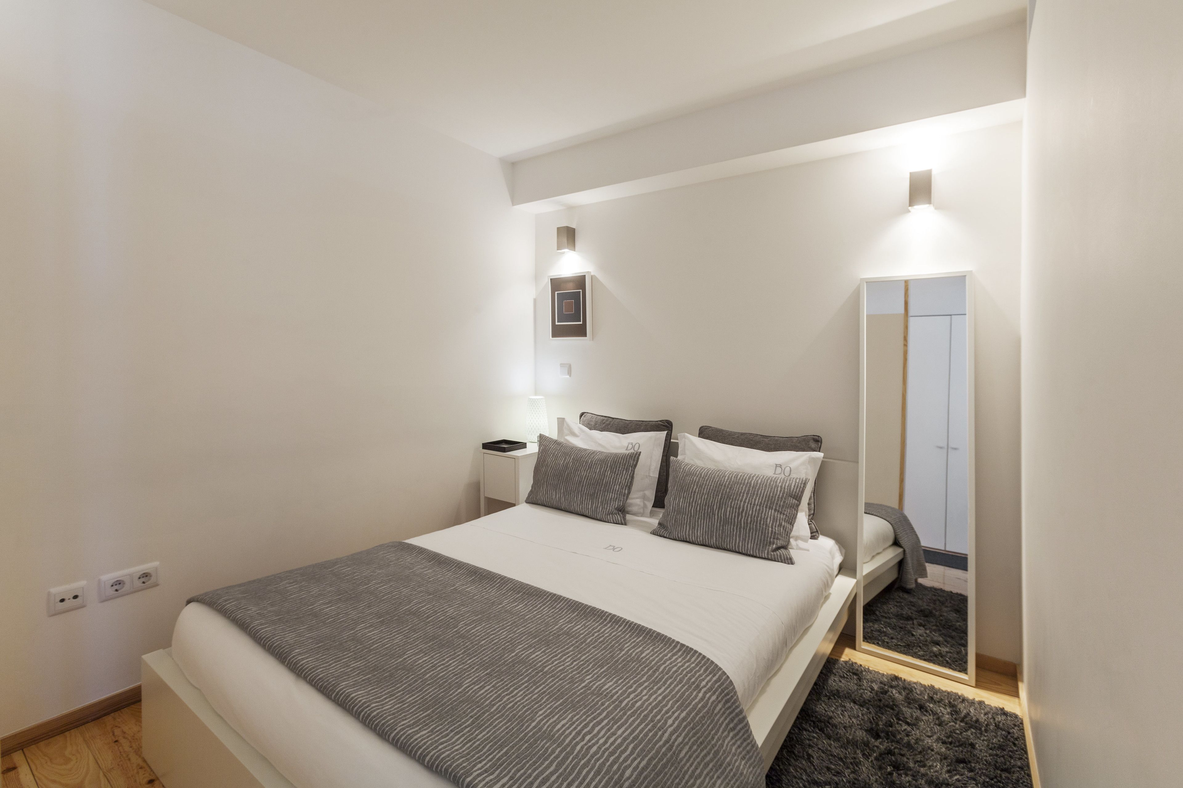 A modern bedroom with a large bed, bedside tables, a mirror, and a wardrobe.