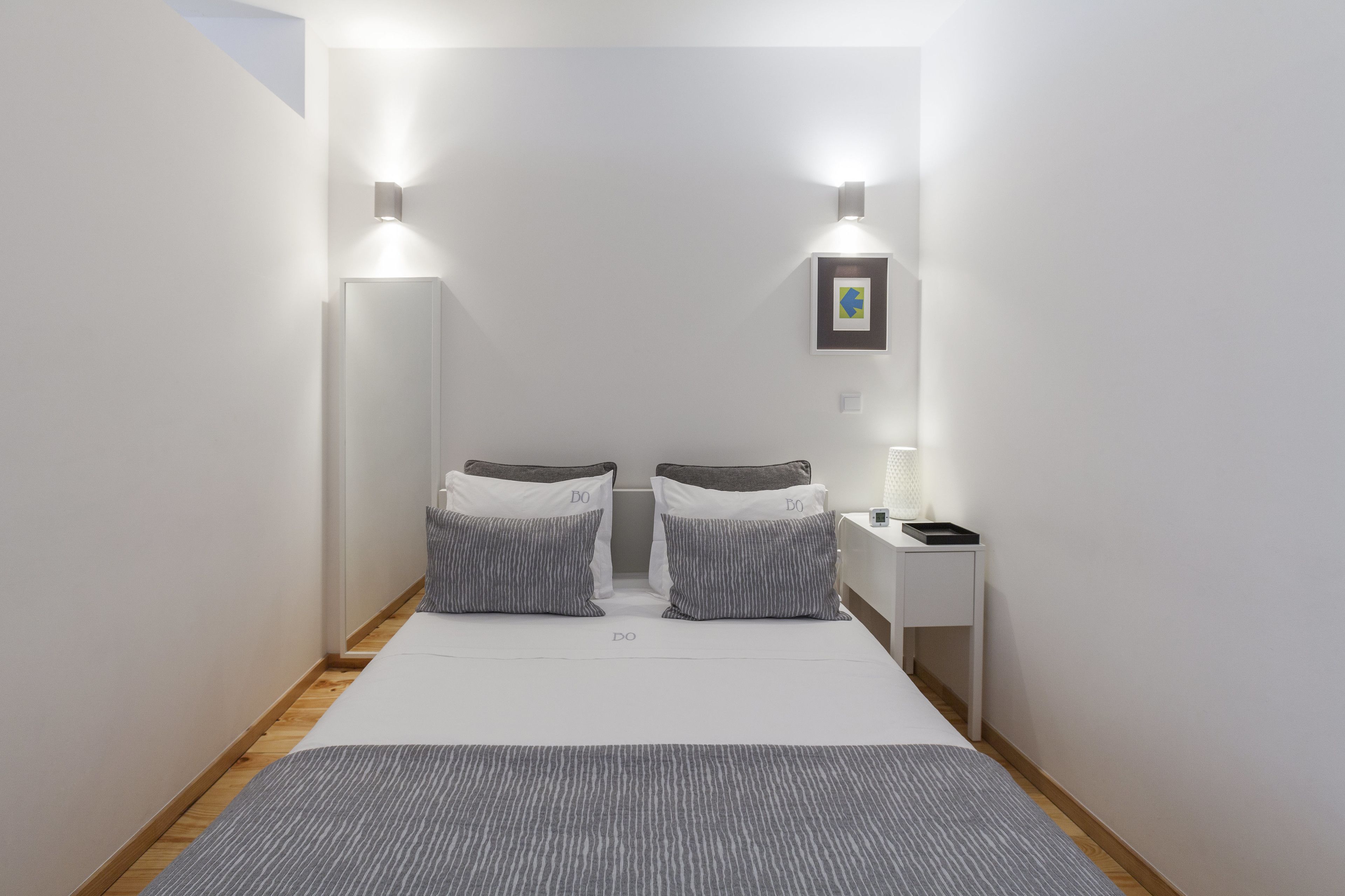 A bedroom with a bed, two bedside tables, a nightstand, and wall-mounted lights.