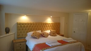 Een slaapkamer met een gestoffeerd hoofdeinde, een bed met witte lakens, meerdere kussens, een nachtkastje en een nachttafel.