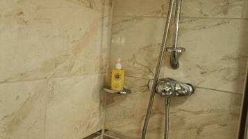 A shower with a handheld showerhead and a fixed showerhead, a yellow soap dispenser on a shelf, and tiled walls.