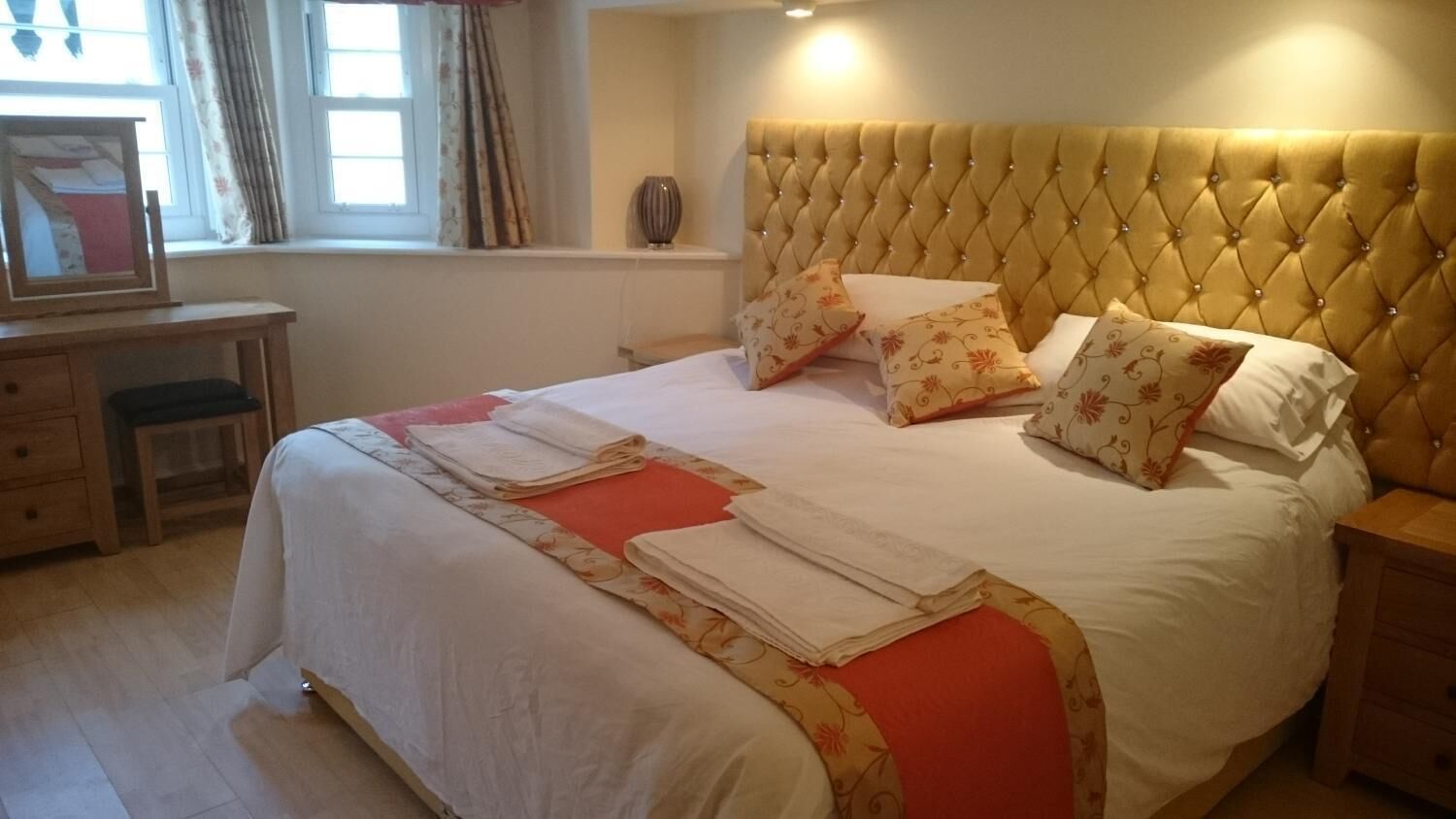 Cama bem arrumada com cabeceira estofada, vários travesseiros e um corredor vermelho decorativo.