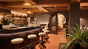 A bar area with stools, a bar counter, and shelves with bottles and glasses. - Hotel Savoy (Badia)
