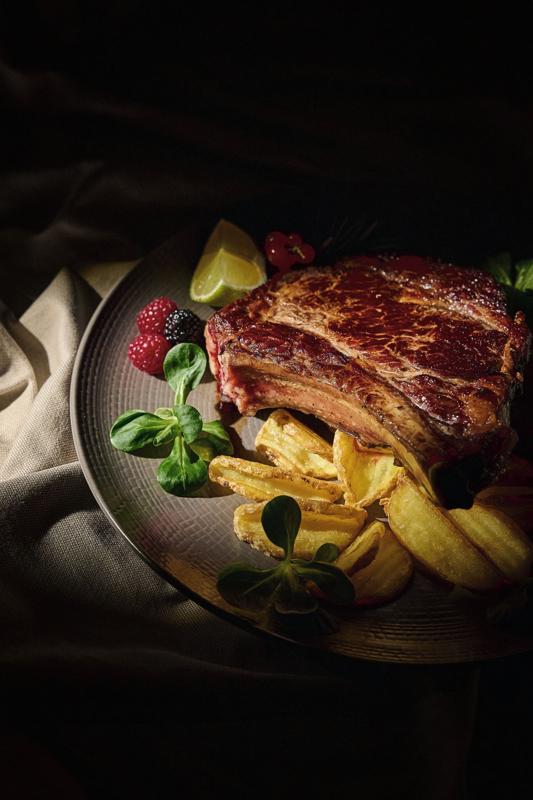 Ein Teller mit einem Steak, Pommes, Beeren und einem Limettenschnitz.