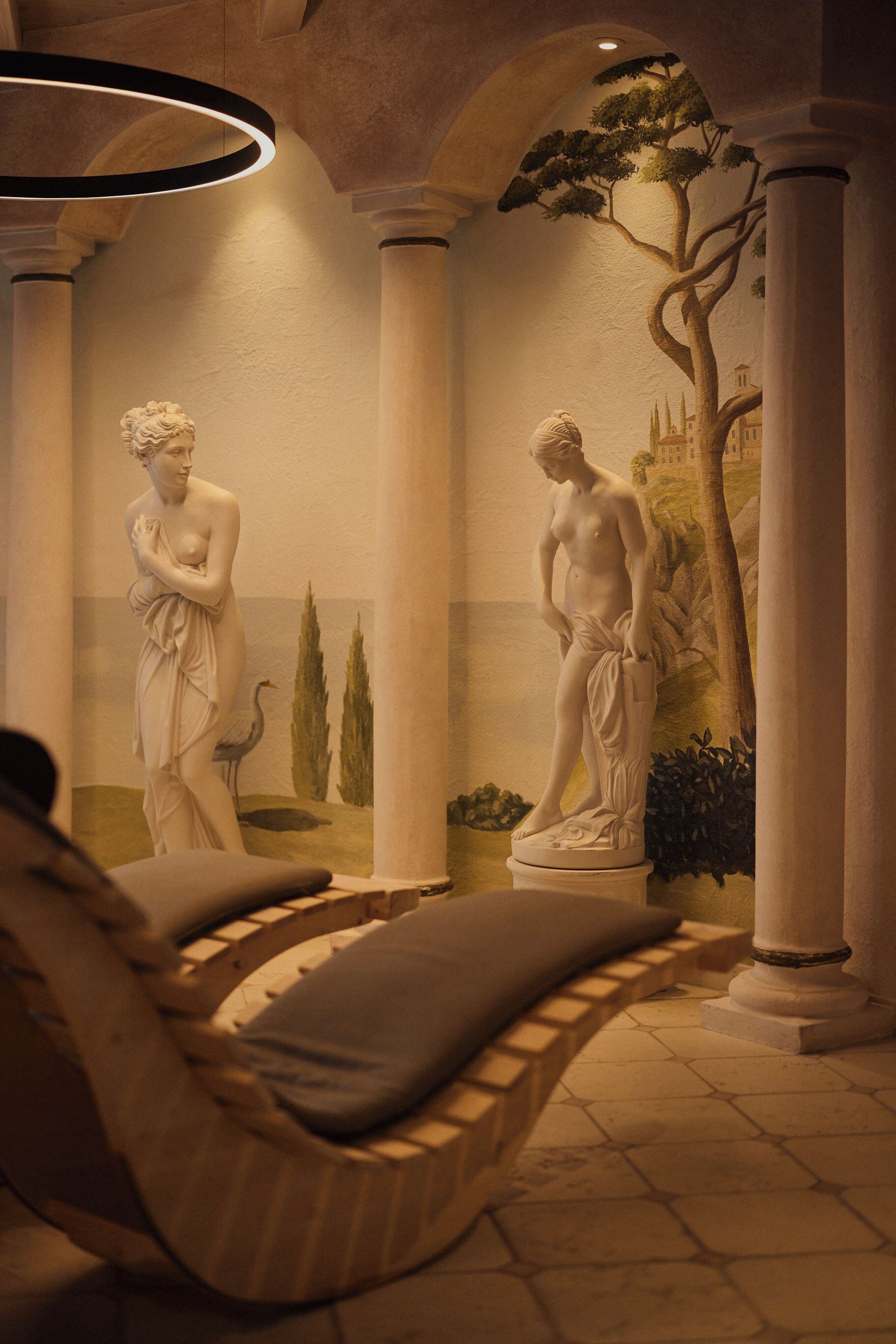 A room with a reclining chair, a mural with classical statues, and a tree with a building in the background.