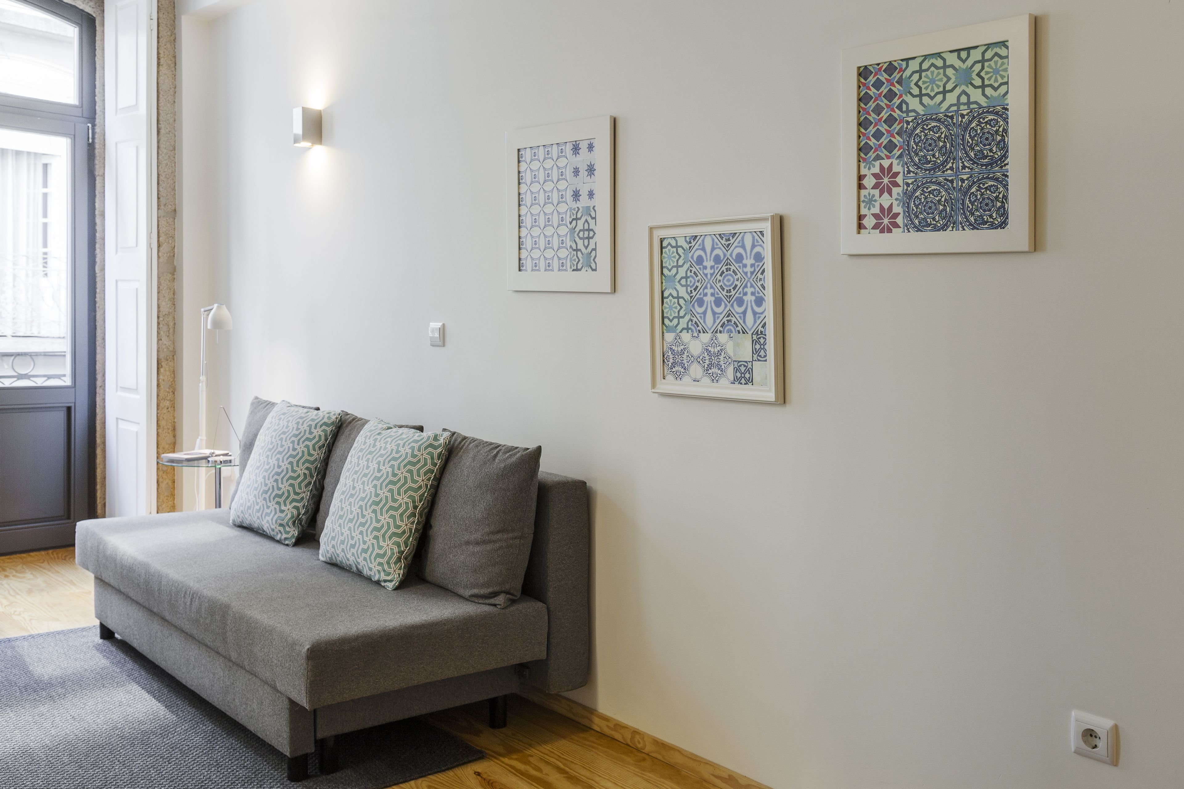 Un salon moderne avec un canapé gris, des coussins à motifs et deux œuvres d’art encadrées accrochées au mur.