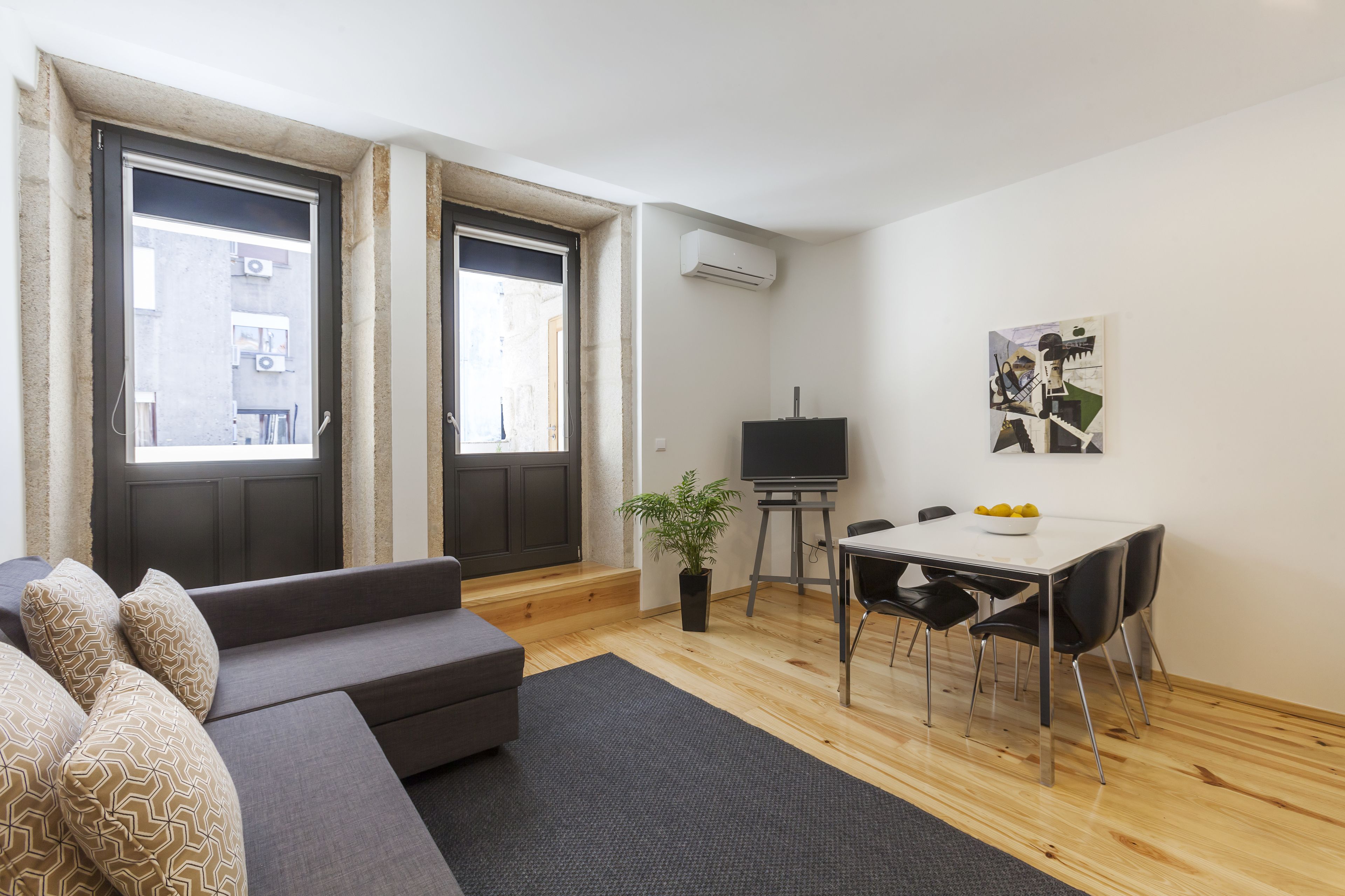 Ein modernes Wohnzimmer mit einer Couch, einem Esstisch mit Stühlen, einer Zimmerpflanze und einem Bild an der Wand.