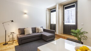 Una sala moderna con un sofá seccional gris, una mesita auxiliar, una lámpara de pie, una mesa de comedor blanca y un cuenco de limones.