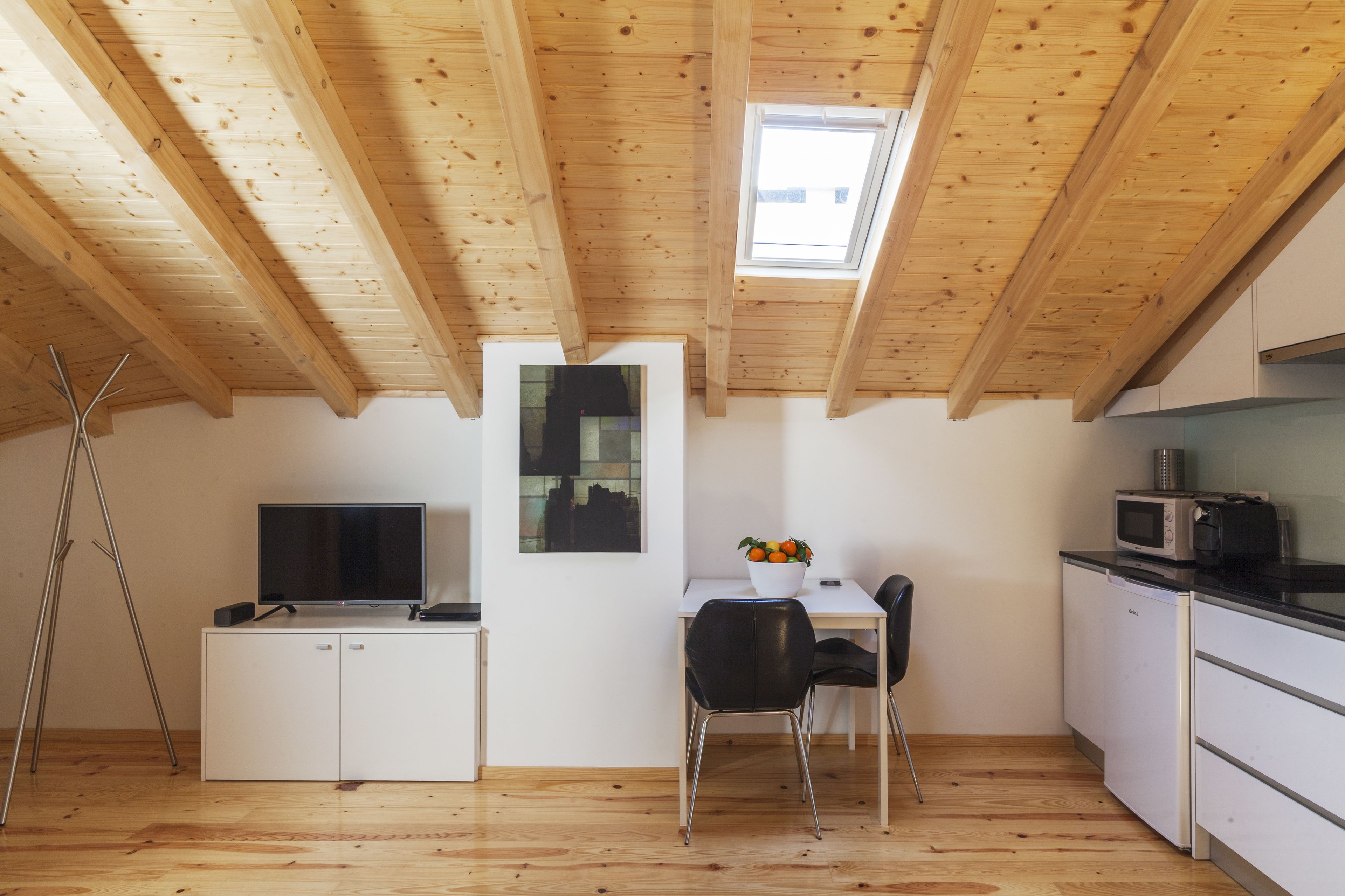 Een compacte keuken met houten balken, een eethoek en een kleine televisie op een kast.