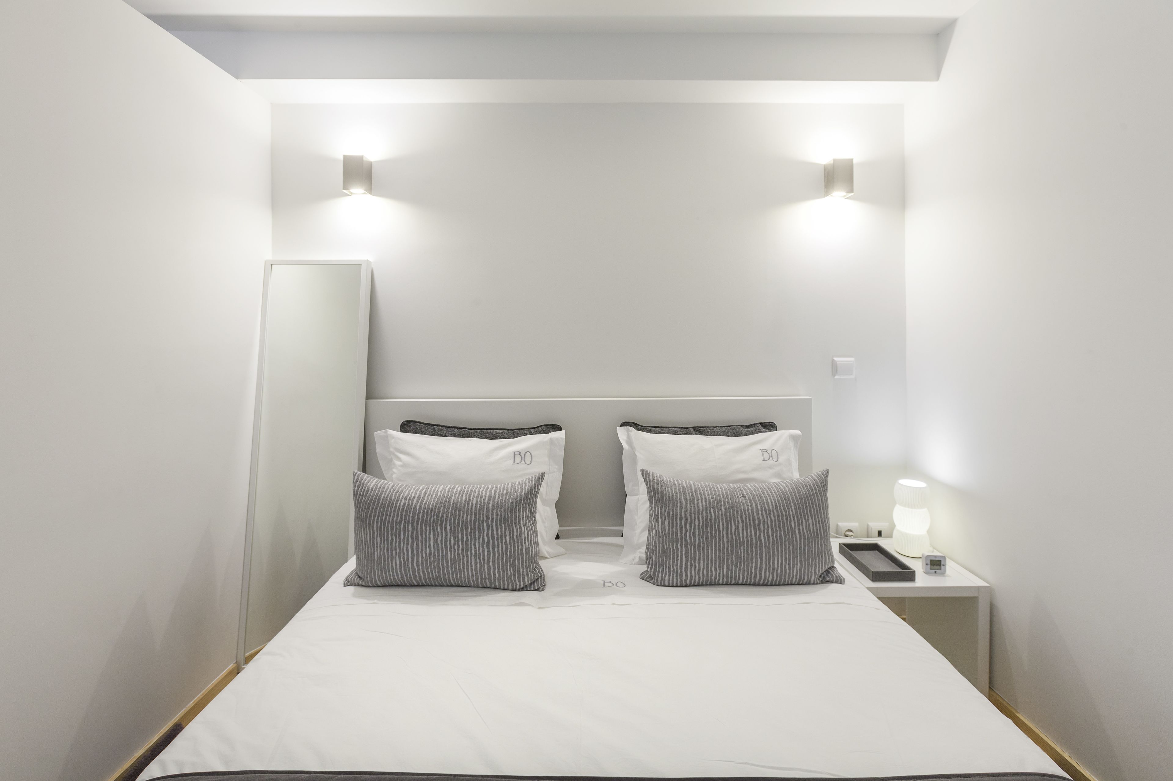 Une chambre d’hôtel moderne avec un grand lit, deux tables de chevet, une petite table et un miroir.