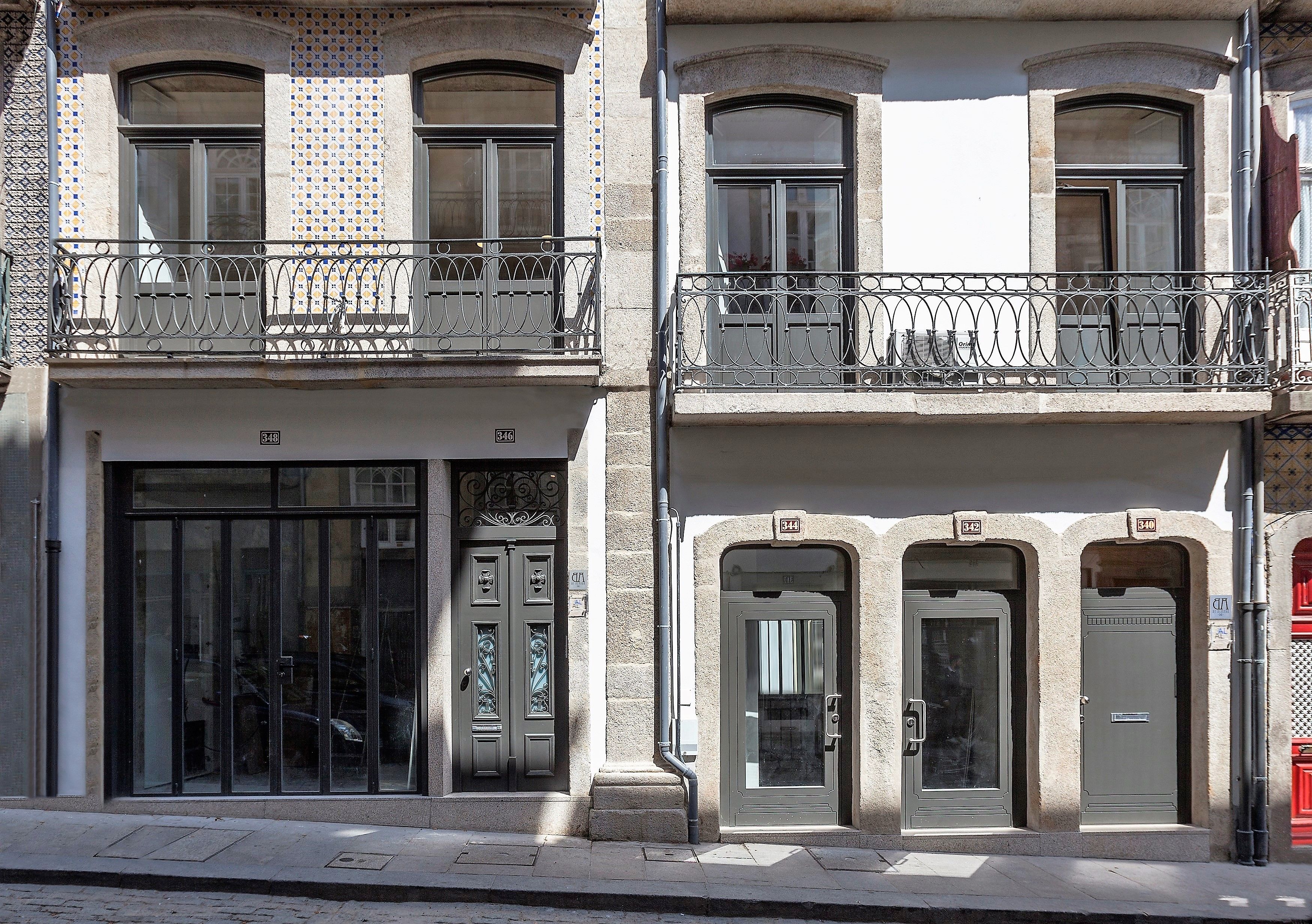 Un edificio con entrada a nivel de calle, balcones en los pisos superiores con barandillas de hierro forjado y fachada con tejas.