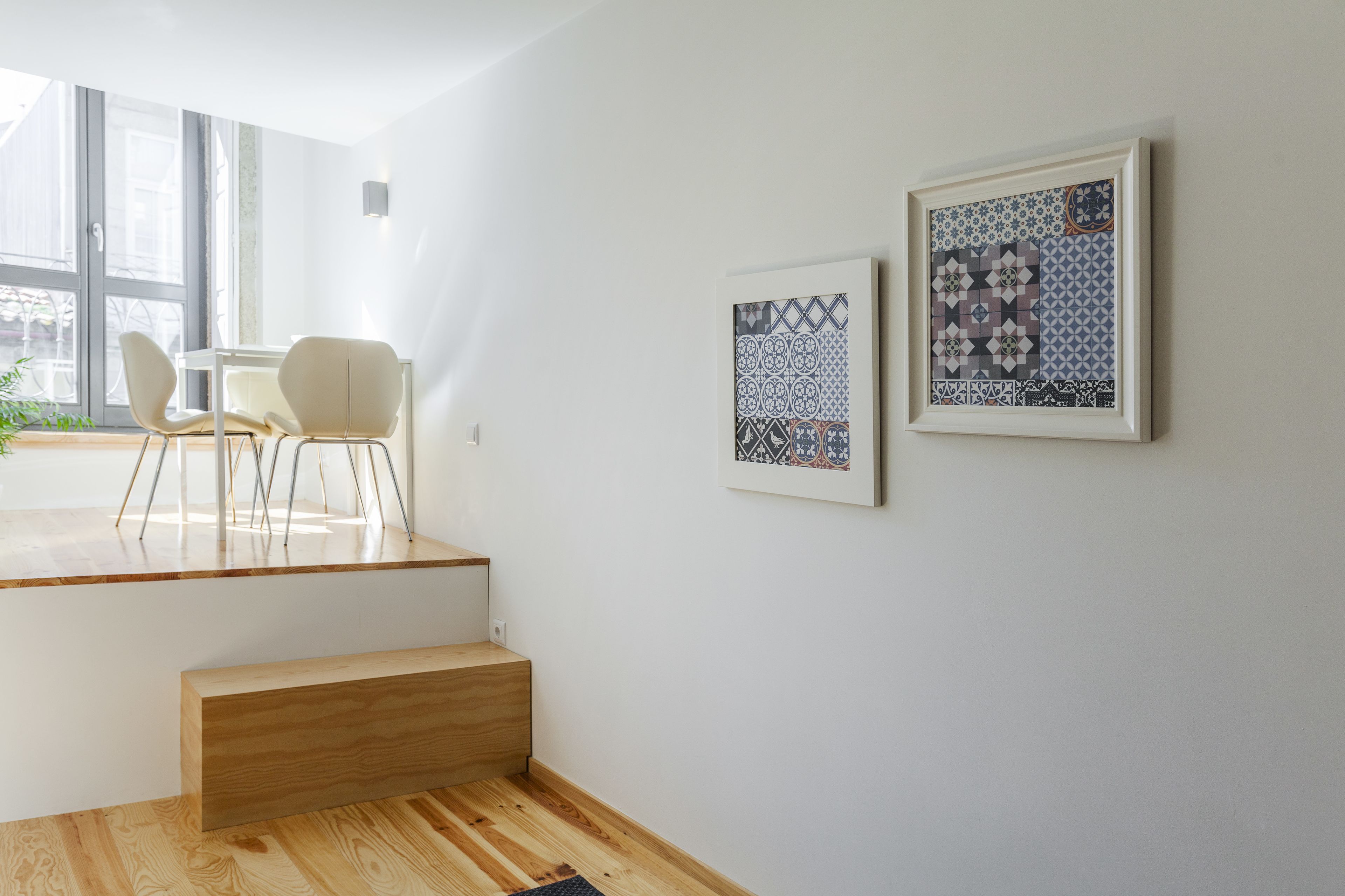 Quarto moderno com escada de madeira, área de jantar com cadeiras e duas obras de arte emolduradas na parede.