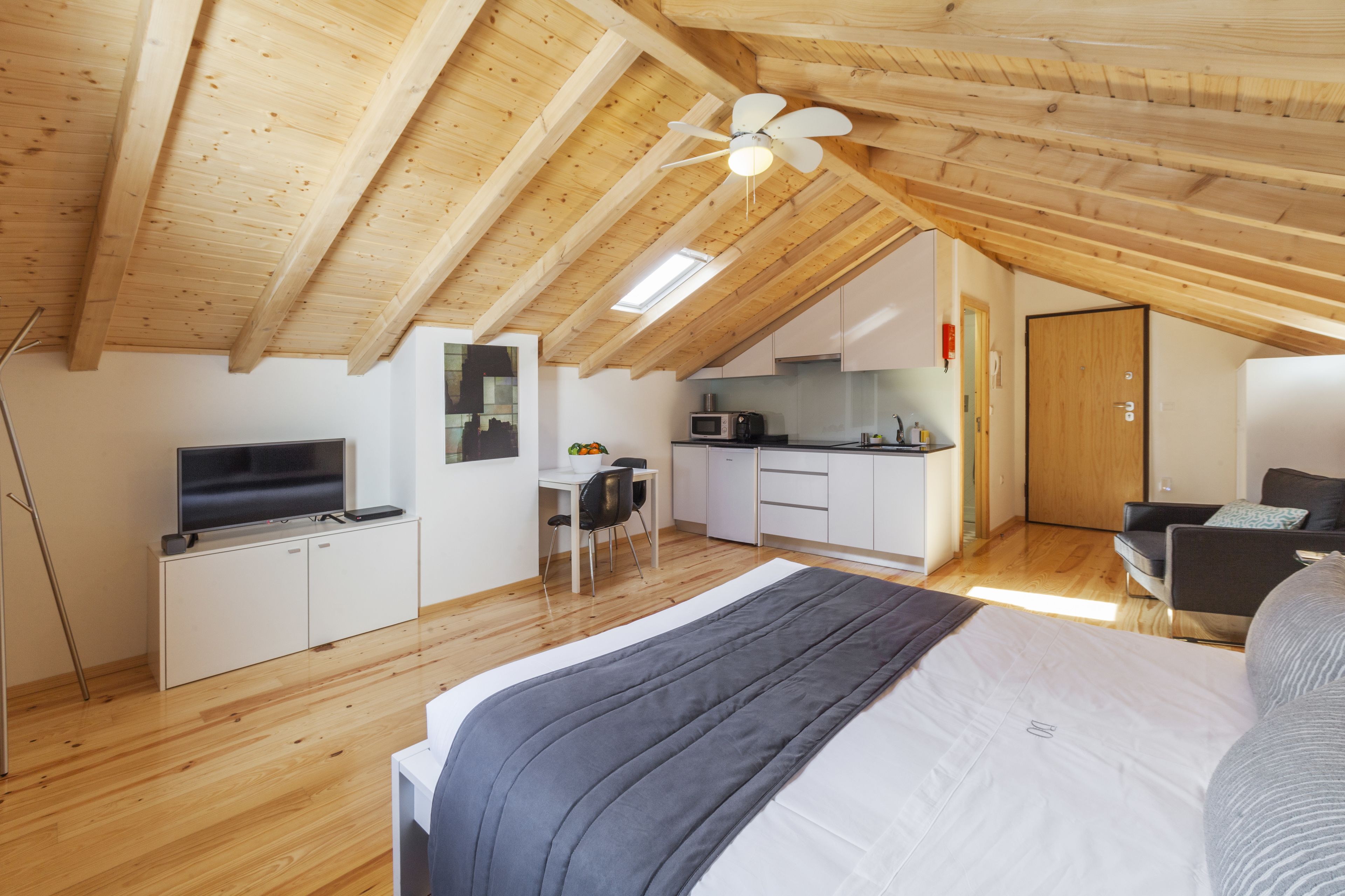 Een compact, modern loft appartement met een schuine kap, een kitchenette, een eethoek en een slaapkamer met een groot bed.