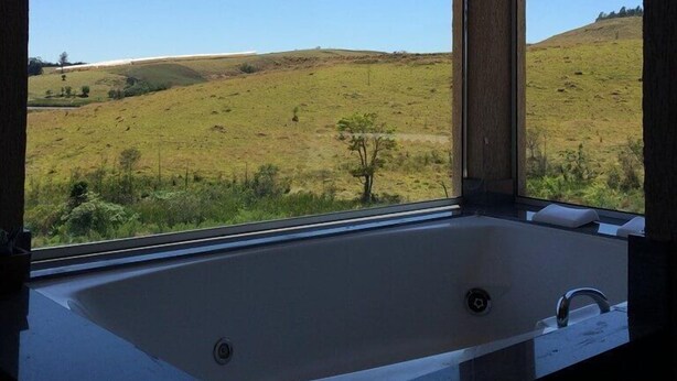 A bathroom with a large window offering a view of a grassy landscape. - Hotel Fazenda Santa Maria (Serra Negra)