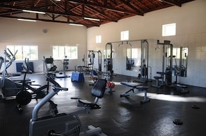 Une salle de sport spacieuse, dotée de divers appareils d’entraînement, de grandes fenêtres et d’un plafond haut.