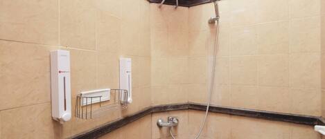 Ein Badezimmer mit beigen Fliesen, einer Dusche, einer Toilette und einem Heizkörper.