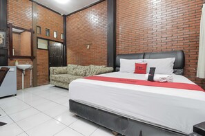 A hotel room with a brick wall, a bed with white bedding and red accents, a sofa, and a small table with a sink. - RedDoorz @ Cilandak Timur (Jakarta)