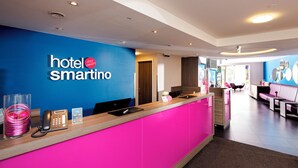 A hotel reception desk with a blue wall, a phone, a digital screen, and a counter. - Hotel Smartino (Schwäbisch Hall)
