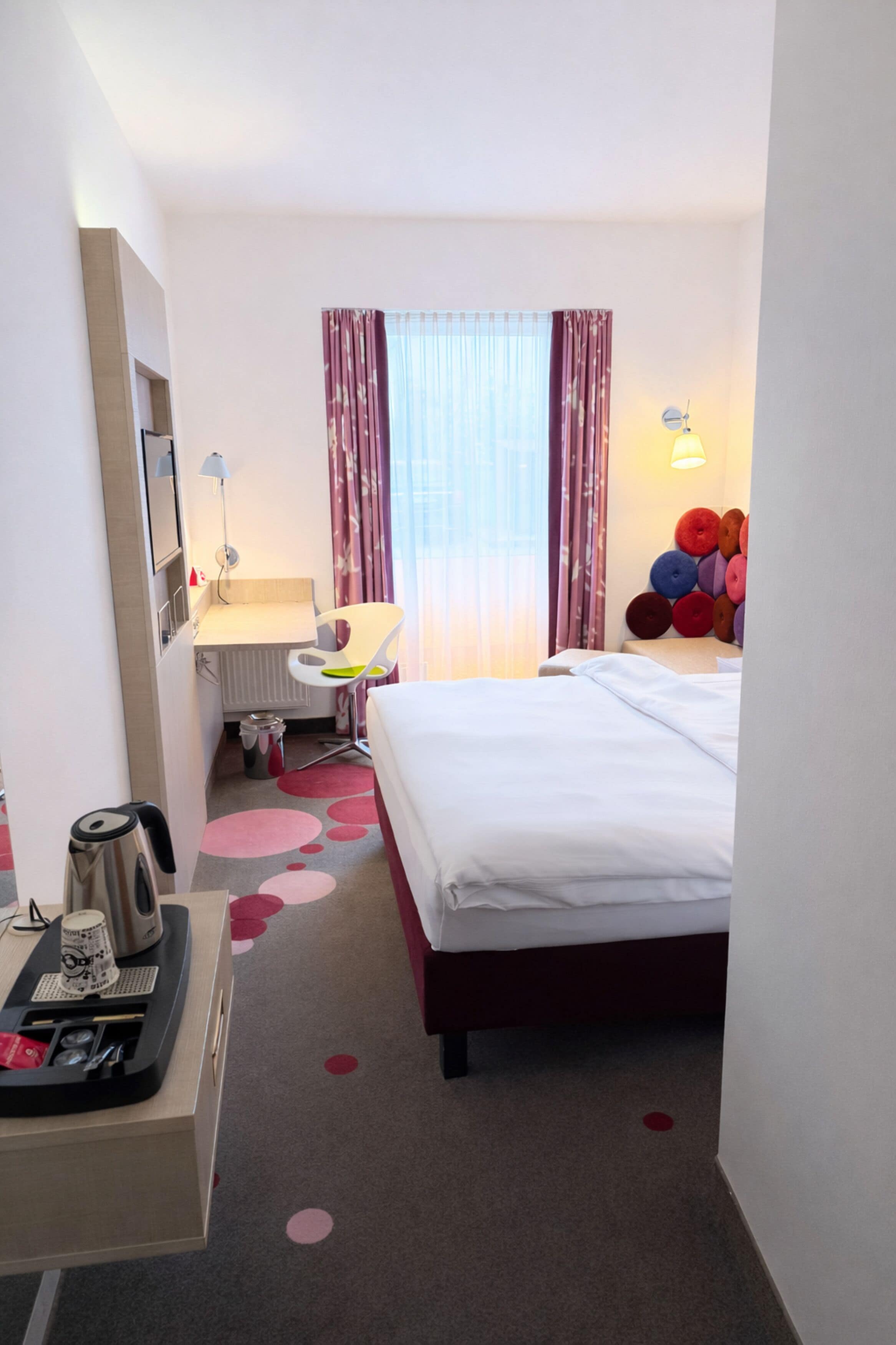 Habitación de hotel con cama, escritorio, silla, radiador, lámpara y un adorno en la pared.