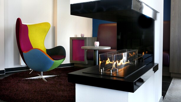 A modern living room with a colorful chair, a black fireplace, and a small table with a pink object. - Hotel Smartino (Schwäbisch Hall)