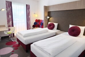 A hotel room with two beds, a desk, a chair, a radiator, and a wall-mounted lamp. - Hotel Smartino (Schwäbisch Hall)