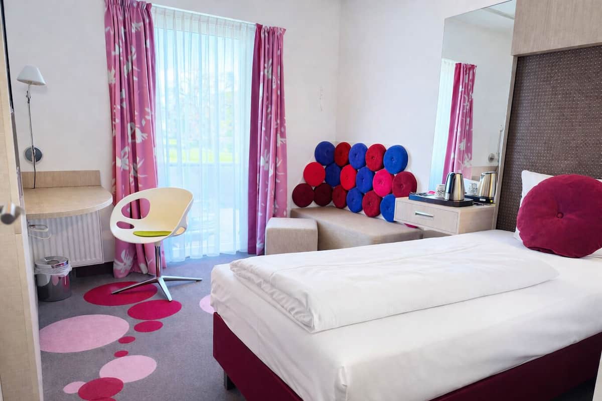 Una habitación de hotel con cama, escritorio, silla, un panel decorativo en la pared y espejo.