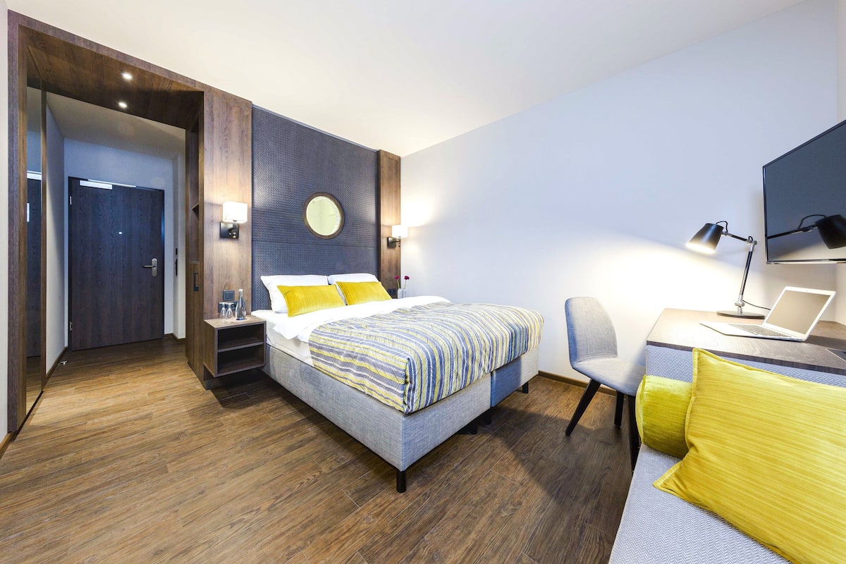 Una habitación de hotel moderna con cama, escritorio, silla y televisor.