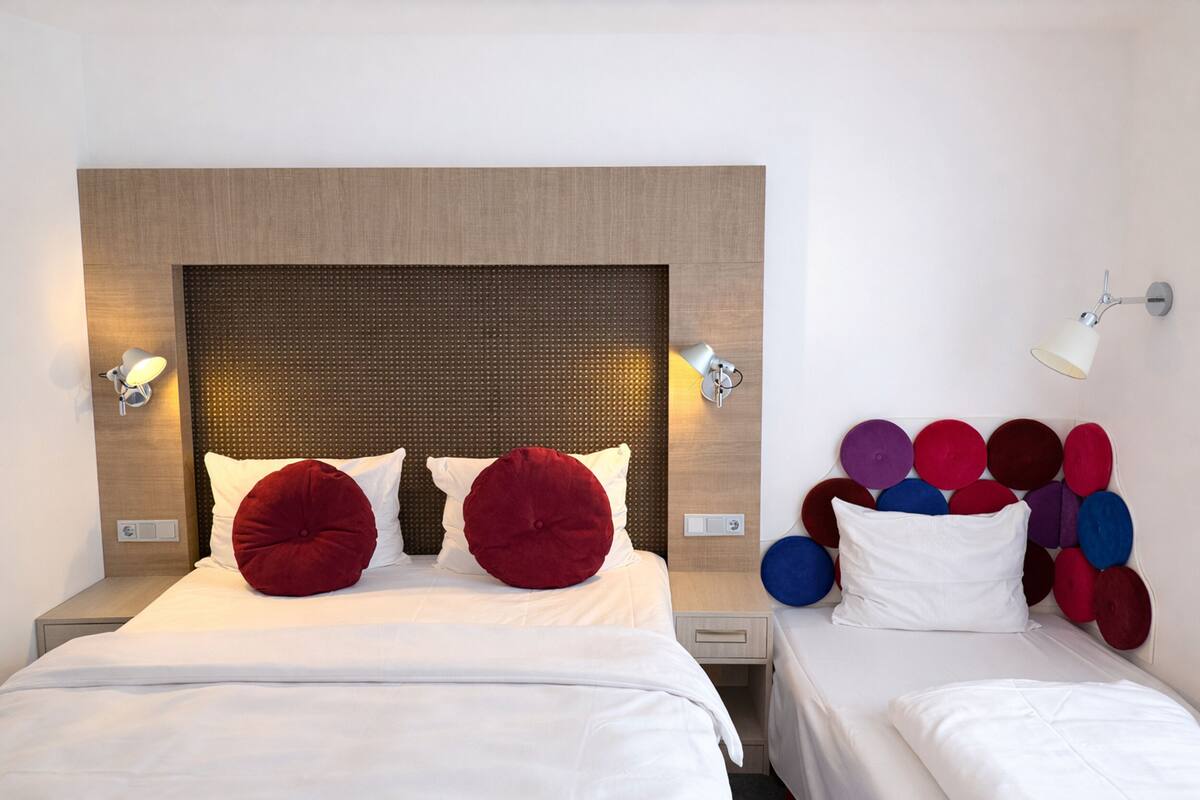 Una habitación de hotel con una cama grande, dos mesitas de noche, una lámpara de pared y un cabecero con textura.