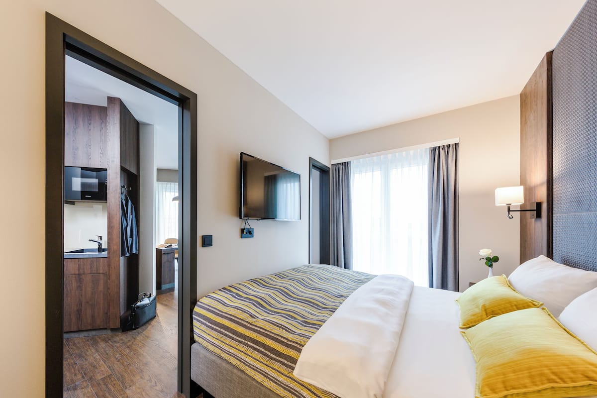 Una habitación de hotel con cama, televisión, escritorio y ventana con cortinas.