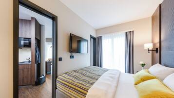A hotel room with a bed, a TV, a desk, and a window with curtains.