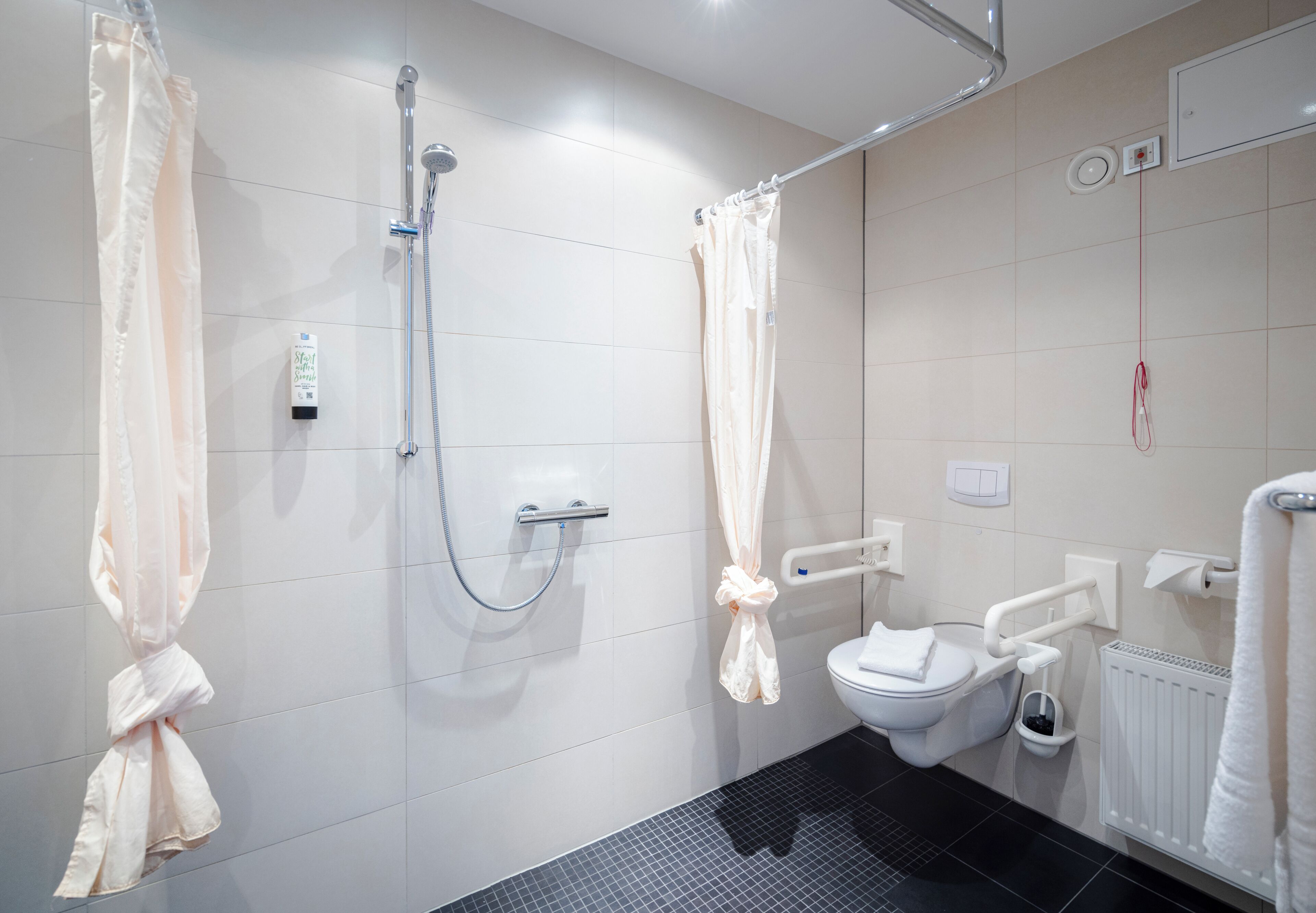 Un baño con ducha, inodoro y barras de apoyo.